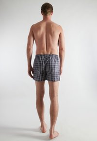 Heren zwemshorts met een ruitpatroon, voorzien van een elastische tailleband, voornamelijk in marineblauw met een lichtblauw, wit en grijs ruitpatroon, gemaakt van lichtgewicht stof.