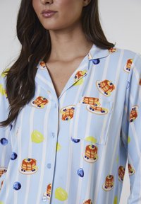 Blaue und weiße gestreifte Schlafanzüge mit einem Pfannkuchen- und Obstmuster. Hergestellt aus leichtem Stoff mit einer Brusttasche und Knopfdetails.