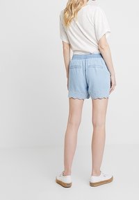 Shorts bleu clair avec un ourlet texturé, une ceinture élastique et deux poches arrière ; portés avec un haut blanc ample à manches courtes et des baskets.