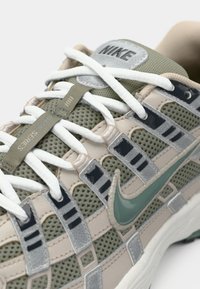 Sneakers Nike z siateczkową cholewką w beżowym i zielonym kolorze, z szarymi akcentami, białymi sznurowadłami oraz wyraźnym zielonym logo swoosh z boku.