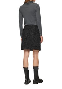 Haut à manches longues gris associé à une jupe noire texturée. Bottines noires avec des chaussettes côtelées. Accent sur les détails du tissu et de la silhouette.