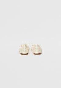 Zapatos de cordones de color crema claro con un diseño de tejido texturizado y una pequeña suela marrón. Presentan un lazo en la parte trasera como detalle.