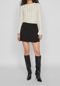 Krämfärgad stickad långärmad topp med vertikala randar, svart omlottkjol och knähöga svarta klackstövlar. Slät tyg, skräddarsydd passform och utsvängda ärmar.