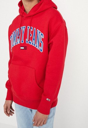 Sweat à capuche rouge avec "TOMMY JEANS" en lettres bleues et blanches sur la poitrine, poche avant et petit logo sur le bord de la manche.