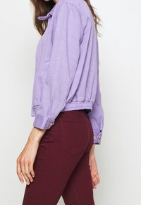 Veste cropped lavande avec un col arrondi, une taille élastique et des poignets boutonnés ; associée à un pantalon ajusté bourgogne avec des poches arrière.