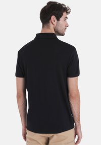 Zwarte polo-shirt van glad katoen, met een klassieke kraag en korte mouwen, een licht gebogen zoom en een minimale merkvermelding.