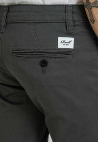 Graue Baumwollhose mit Seitentasche und sichtbarem Markenlabel. Der Stoff hat eine glatte Textur und einen klassischen Schnitt.