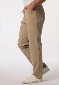 Beżowe spodnie wykonane z miękkiego materiału charakteryzują się luźnym krojem, bocznymi kieszeniami i elastycznym paskiem, zestawione z białymi trampkami.