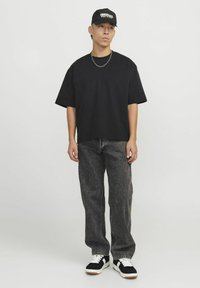 Crna oversized majica, sive traperice, crne tenisice s bijelim detaljima i crna kapa s natpisom "ORIGINALS" u bijelom.