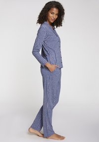 Navy pidžama set napravljen od mekog materijala s tankim ružičastim vertikalnim prugama, s košuljom na gumbe i ravnim hlačama s bočnim džepovima.