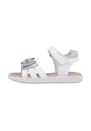 Sandal blanca con detalles plateados, presenta un lazo decorativo, diseño abierto y tres tiras. Suela de goma con agarre texturizado. Cierre de velcro.
