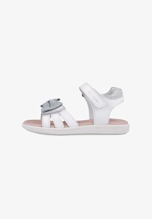 Sandal blanca con detalles plateados, presenta un lazo decorativo, diseño abierto y tres tiras. Suela de goma con agarre texturizado. Cierre de velcro.