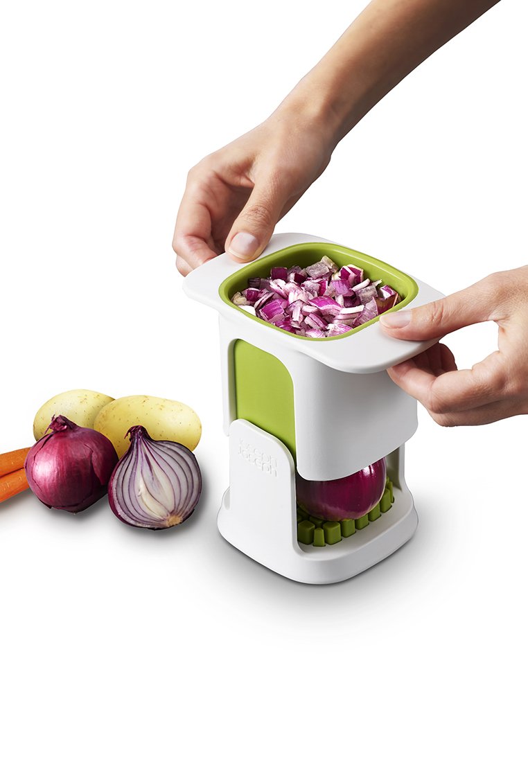 Uienhakker in wit en groen plastic, met gesneden rode ui erin. Verse groenten, waaronder paarse en gele uien, aardappelen en wortelen in de buurt.