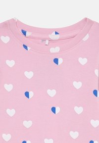 Rosa bomullströja med ett mönster av vita och blå hjärtan. Urringningen är rundad med en slät textur och korta ärmar.