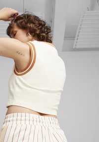 Top cropped bianco con bordi a coste marroni, abbinato a pantaloni corti bianchi con righe sottili. Il tessuto appare morbido, con un design aderente.
