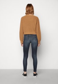 Suéter de punto corto en marrón, leggings azul oscuro con bolsillos traseros y zapatos negros sin cordones. Textura suave, ajuste casual y diseño minimalista.