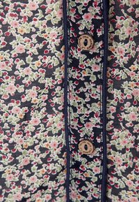 Tessuto a fantasia floreale in blu navy con fiori rosa e verdi. Presenta un bottone di legno e un bordo a contrasto lungo il margine.