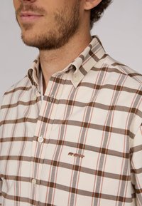 Chemise boutonnée crème avec un motif en tartan marron et rouge ; présente un patch de trois ours brodés près de la poche poitrine. Tissu en coton.