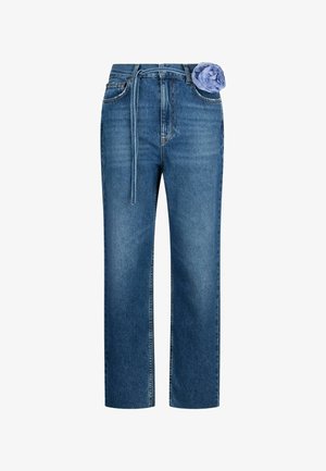 Mėlyni džinsai tiesiomis kojomis su audinio diržu ir šviesiai violetine audinio gėle, pritvirtinta prie juosmens juostos.