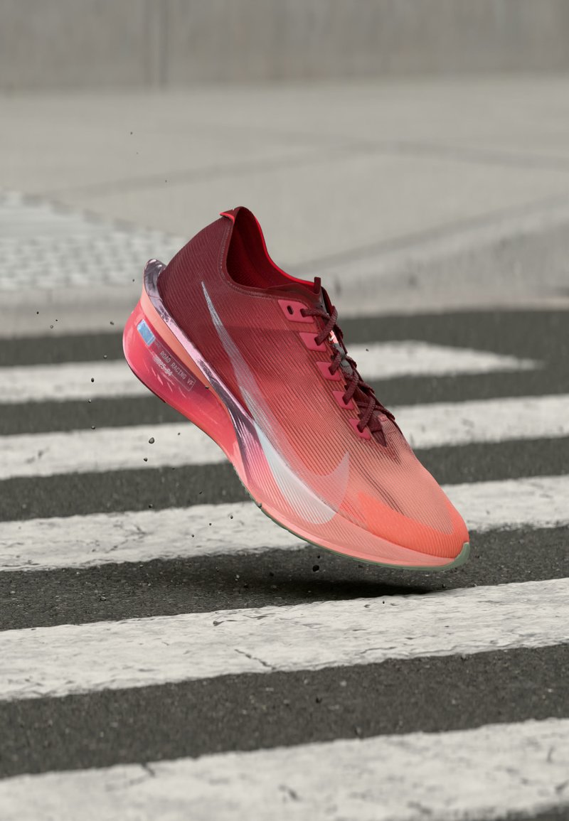 Κόκκινο και ροζ παπούτσι για τρέξιμο Nike με κορδόνια, αιωρούμενο πάνω από διάβαση πεζών σε ασφαλτοστρωμένο δρόμο.