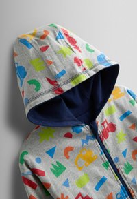 Šedá mikina s kapucňou s farebnými geometrickými vzormi v červenej, modrej, zelenej a žltej farbe. Tmavomodré lemovanie okolo kapucne a zipsu.