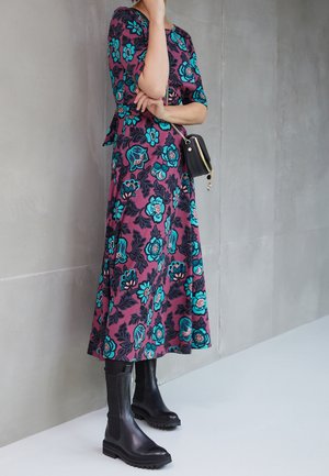 Floral print dress in dark purple with turquoise and black flowers; paired with black knee-high boots and a small black handbag.
