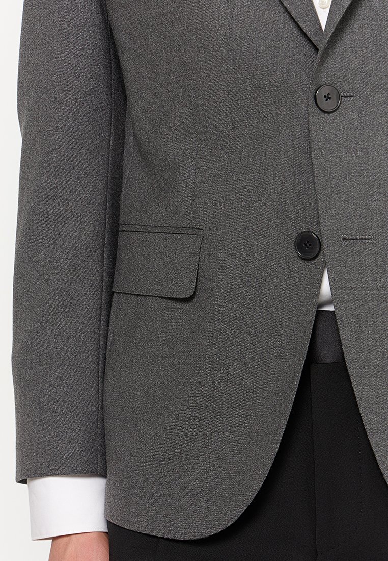 Blazer gris en tissu texturé, doté d'une fermeture à deux boutons, de revers crantés et d'une poche poitrine simple. Manches de chemise blanche visibles.