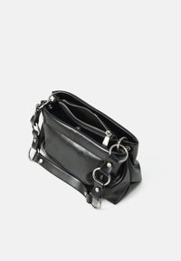 Sac à main en cuir noir avec des accents en anneaux argentés et un compartiment principal zippé partiellement ouvert sur un fond blanc.