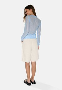 Ljusblå långärmad topp med en texturerad yta och scalloped nederkant, kombinerad med beige linneshorts och svarta plattformssandaler.