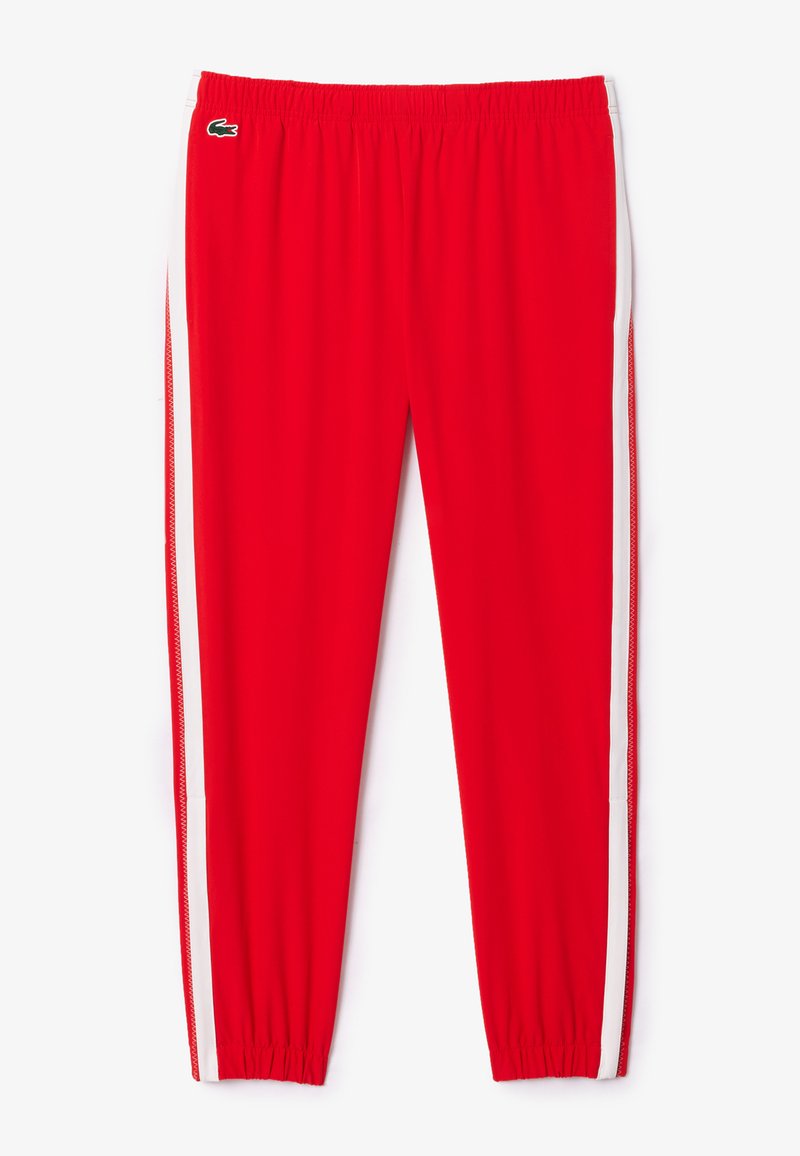 Un pantalon de sport rouge en tissu respirant, avec une taille élastique et des rayures blanches sur les côtés, comportant un petit logo près de la taille.