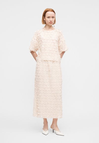Ροζ ανοιχτό ρούχο δύο τεμαχίων με κοντομάνικο τοπ και μακριά φούστα, διακοσμημένο με υφασμάτινα λουλουδένια στολίδια.