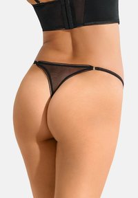 String noir en mesh avec des fines bretelles, un design minimaliste et une texture légère. Détail en anneau inséré à l'arrière qui accentue la silhouette.