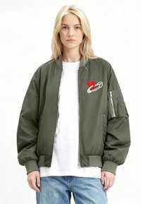 Olivengroene bomberjack met een borduursel van een hart en veiligheidsspeld, geribbelde manchetten en zoom, en een met rits afsluitbaar zakje op de mouw.