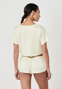Helles gelbes Crop-Top und Shorts-Set, mit weicher Textur und subtilen Mustern. Verstellbarer Knoten am Taillenbund, lockere Passform der Ärmel.