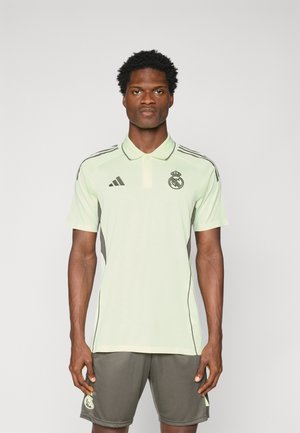 Polo shirt de sport vert clair avec un col, accents latéraux gris foncé et logo du Real Madrid. Porté avec un short gris foncé assorti.