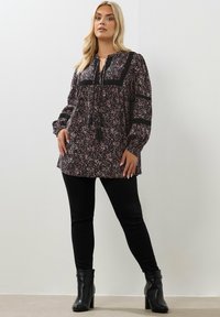 Tunica nera floreale con maniche lunghe, caratterizzata da un nodo e frange al collo. Abbinata a pantaloni aderenti neri e stivaletti.