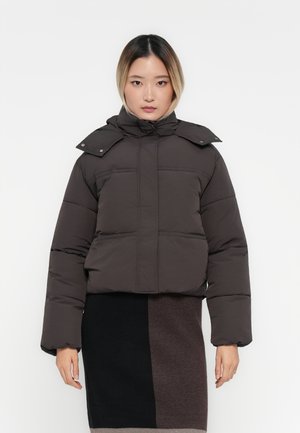 Kort donkerbruin pufferjack met een hoge kraag, zichtbare stiksels en drukknoopjes. Gecombineerd met een multi-getinte gebreide rok.