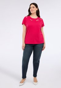 Fuksia lyhythihainen t-paita, jossa on kirjailtu kukkakuvio kaula-aukolla, yhdistetty tummiin farkkuihin ja valkoisiin korkokenkiin.