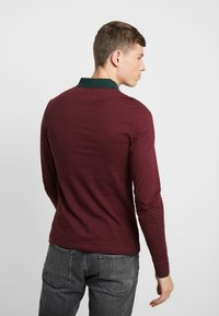 Polo à manches longues bordeaux avec un col vert, en coton, présentant une coupe ajustée et des coutures minimales à l'arrière.
