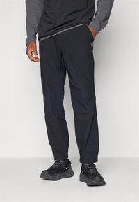 Schwarze, leichte Outdoor-Hosen mit lockerer Passform, ausgestattet mit siden Taschen und dezenten Nähdetails, kombiniert mit schwarzen Sportschuhen.