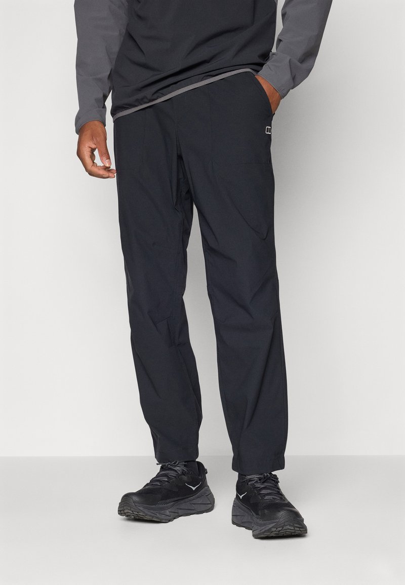 Schwarze, leichte Outdoor-Hosen mit lockerer Passform, ausgestattet mit siden Taschen und dezenten Nähdetails, kombiniert mit schwarzen Sportschuhen.