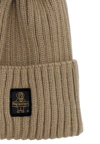 Beanie lavorato a maglia marrone con texture a coste, con un'etichetta nera sul davanti con scritte dorate e una grafica di un cane.