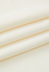 Tissu couleur crème avec une texture lisse, arborant de subtils motifs diagonaux et plié en couches, mettant en valeur sa surface douce et uniforme.