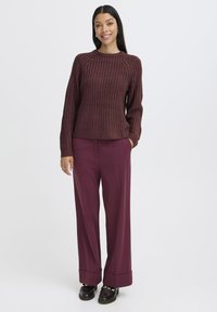 Bordeauxfarbener Strickpullover mit gerippter Textur, kombiniert mit plissierten, weit geschnittenen Pflaumenhosen und schwarzen Schuhen.