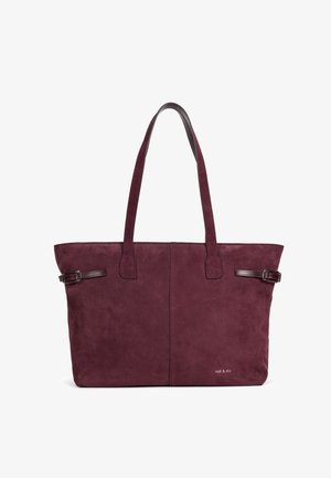 Grand sac cabas en daim bordeaux avec deux longues anses, détails de boucles sur les côtés et un petit logo "nat & nin" en bas à droite.