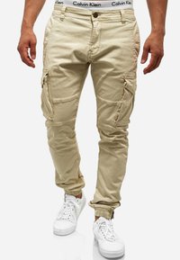 Pantalons cargo beiges avec des poignets élastiques, plusieurs poches latérales et une ceinture Calvin Klein. Fabriqués en tissu doux et texturé.
