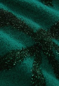 Türkisfarbener Stoff mit einer weichen Stricktextur, akzentuiert mit einem dunklen, glänzenden, flauschigen Material, das in wellenförmigen Linien über den Stoff angeordnet ist.