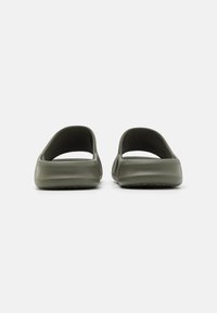 Bottes en plastique vertes à enfiler avec un dos ouvert et des côtés larges, présentant une texture lisse et un talon légèrement surélevé. Design profil bas.