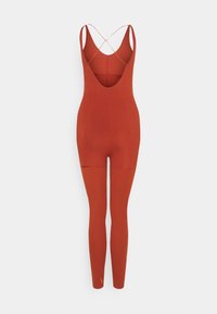 Combinaison sans manches couleur rouille avec des bretelles croisées, corsage ajusté et jambes longues se prolongeant jusqu'aux chevilles.