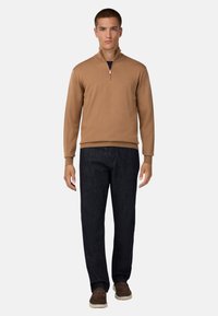 Tan zip-neck tröja med ribbad muddar, kombinerad med mörk denimbyxor och bruna mockaskor. Minimalistisk design, avslappnad passform.